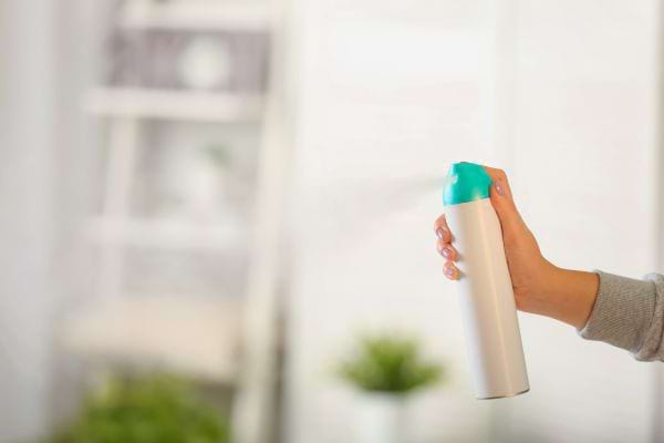 Une main pulvérise un désodorisant en aérosol dans une pièce lumineuse.