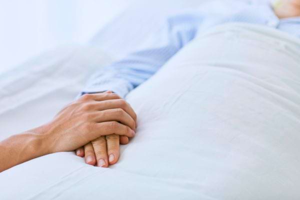 Une main tient tendrement celle d’un patient hospitalisé.