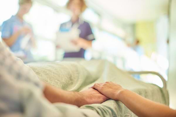 Une main tient tendrement celle d’un patient hospitalisé.