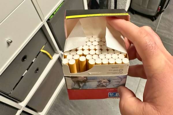 Une main tenant un paquet de cigarettes ouvert, montrant les cigarettes alignées à l’intérieur.