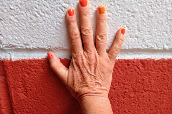 Une main avec vernis orange touche un mur bicolore rouge et blanc.