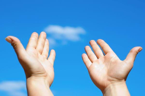 Deux mains levées vers le ciel bleu clair avec quelques nuages.