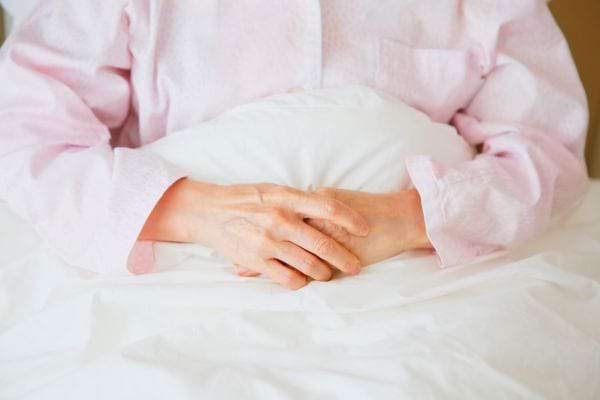 Une personne âgée croise les mains sur sa couverture rose.