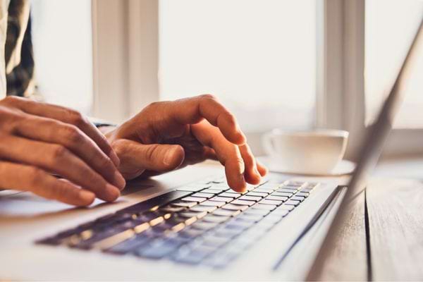 Main tapant sur le clavier d’un ordinateur portable lumineux.