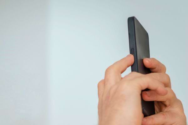 Mains tenant un téléphone noir en position de prise de photo.