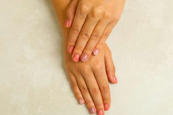 Deux mains bien manucurées aux ongles roses reposent l’une sur l’autre.