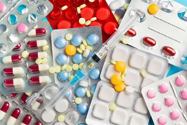 Des comprimés colorés et une seringue posés sur une surface bleue.