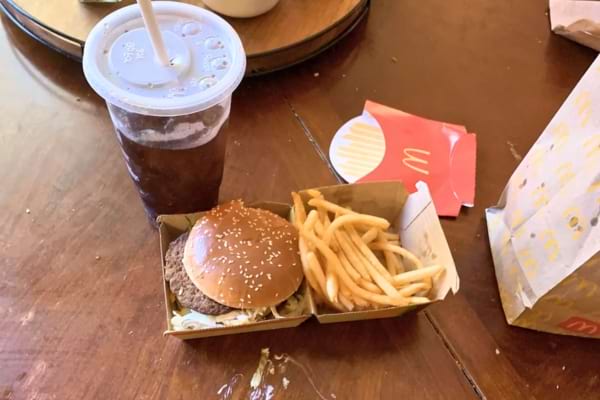 Un menu de fast-food avec un hamburger, des frites et un soda posé sur une table en bois.