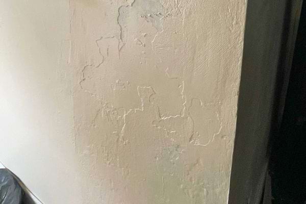 Mur beige présentant des cloques et fissures causées par l’humidité.