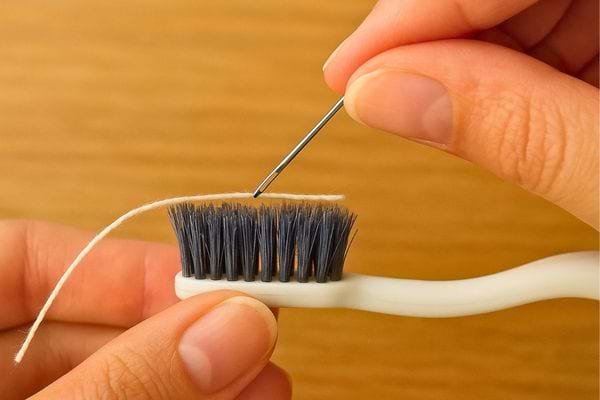 Une main passe un fil sur une brosse à dents pour l’assouplir.
