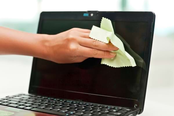 Une main nettoie l’écran d’un ordinateur portable avec un chiffon doux vert.