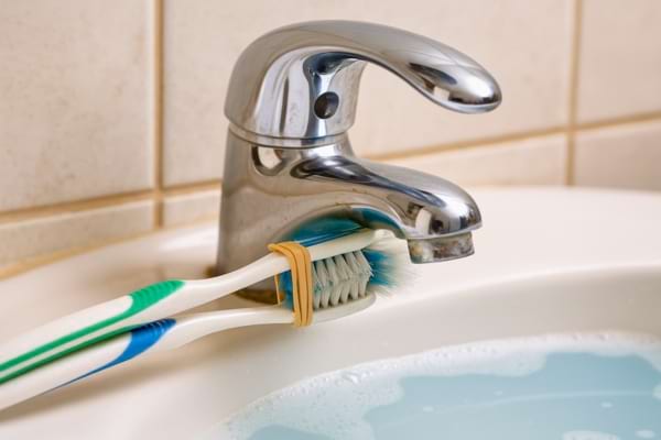 Deux brosses à dents fixées ensemble frottent sous un robinet.