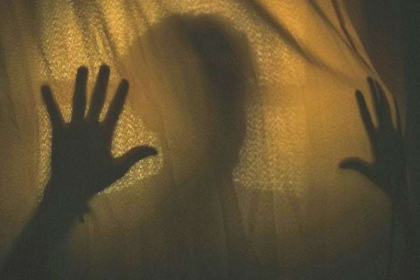 Une ombre humaine apparaît derrière un rideau éclairé avec les mains plaquées contre le tissu.