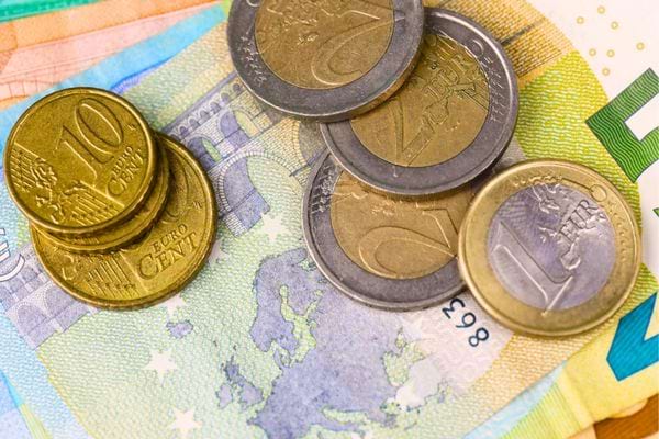 Pièces de monnaie et billets en euros posés sur une surface colorée.