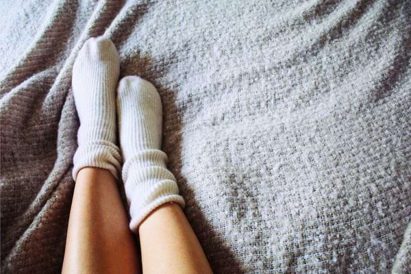 Pieds couverts de chaussettes blanches reposant sur une couverture grise.