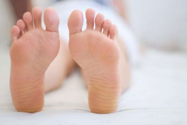 Deux pieds nus reposant sur un lit blanc, vus de près.