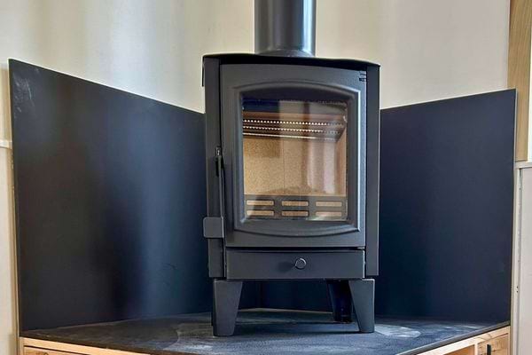 Poêle à bois noir moderne placé dans un coin de mur avec plaques de protection.