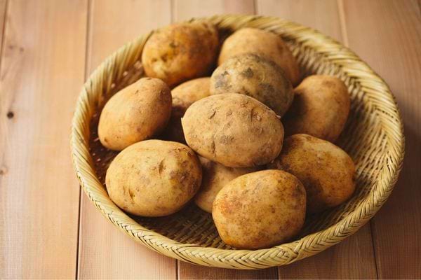 Panier en osier rempli de pommes de terre brutes posées sur une table en bois.
