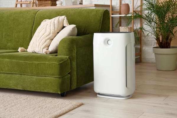 Un purificateur d’air blanc est placé près d’un canapé vert dans un salon lumineux.