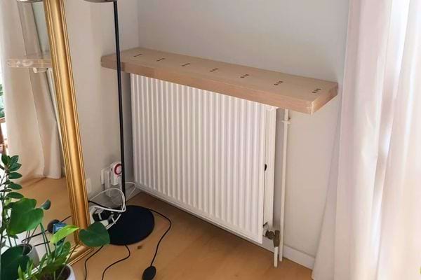 Radiateur blanc recouvert d’une planche en bois dans un coin de pièce.