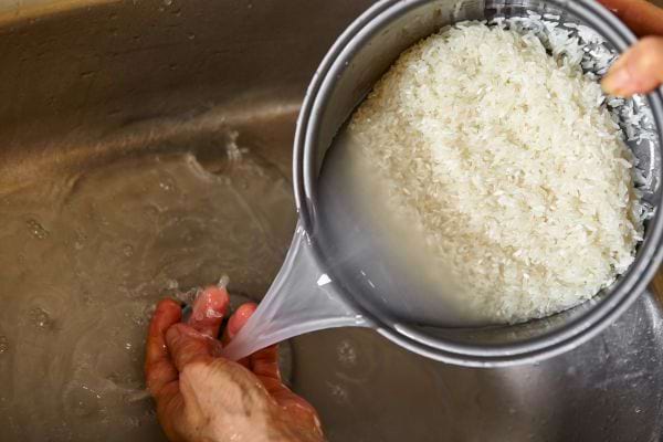 Des mains rincent du riz sous l’eau dans un évier.