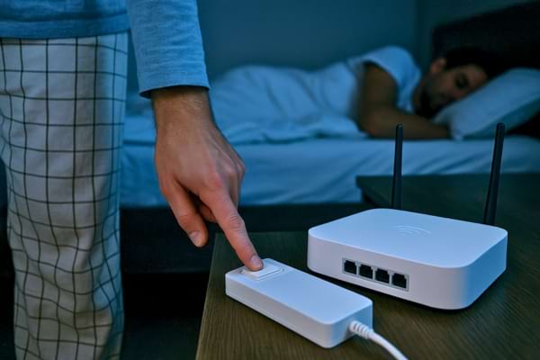 Personne en pyjama éteignant une multiprise ou un routeur Wi-Fi avant de se coucher