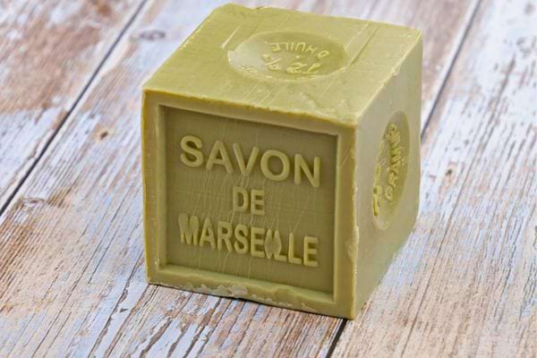 Cube de savon de Marseille vert posé sur une table en bois clair.
