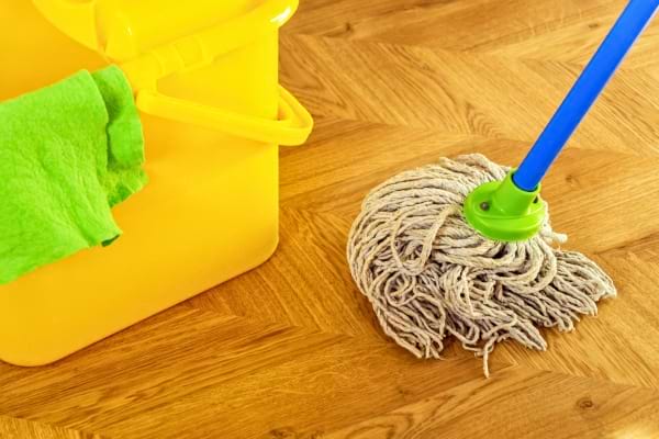 Un seau jaune avec une serpillière repose sur un parquet propre et brillant.