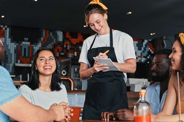 Serveuse souriante prend la commande d’un groupe au restaurant.