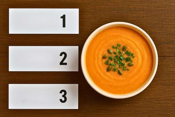 Bol de soupe orange garni de graines et persil, à côté de trois étiquettes numérotées 1, 2, 3.