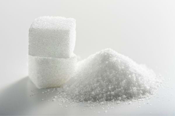 Deux morceaux de sucre blanc posés à côté d’un tas de sucre en poudre.