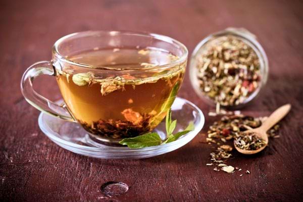 Une tasse de tisane chaude aux herbes, avec un pot d’infusion renversé à côté.