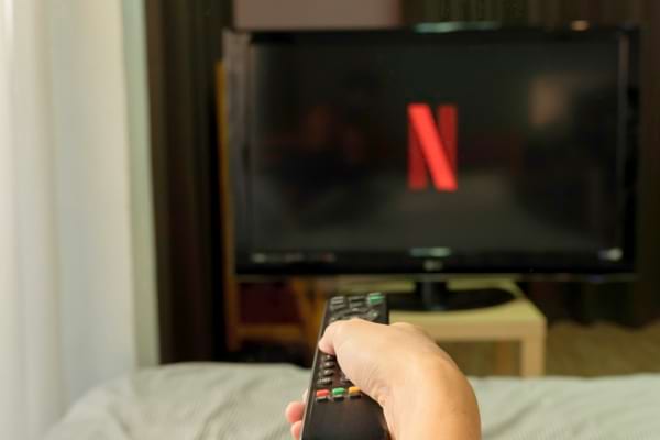 Une main tient une télécommande pointée vers un écran Netflix.