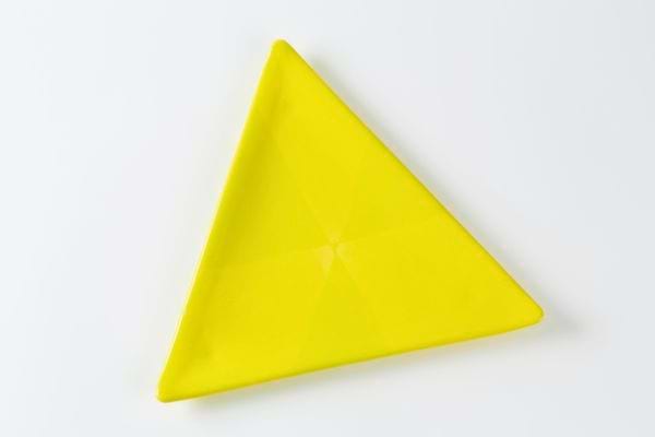 Un triangle jaune en plastique est posé sur un fond blanc.