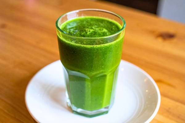 Verre rempli de jus vert posé sur une assiette blanche.