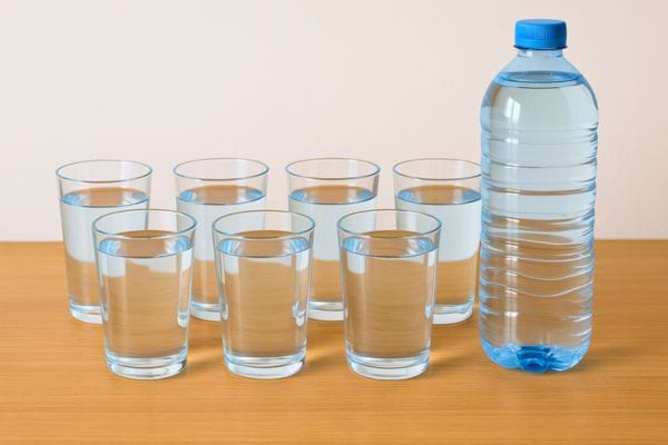Une bouteille d’eau et plusieurs verres remplis alignés sur une table en bois.