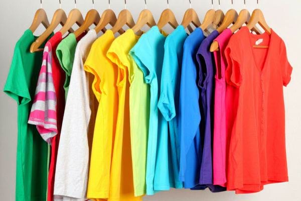 Plusieurs vêtements colorés suspendus sur des cintres, rangés par teinte, illustrant un dressing organisé.