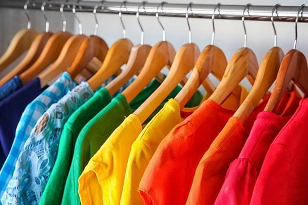 Rangée de vêtements colorés suspendus sur des cintres en bois.