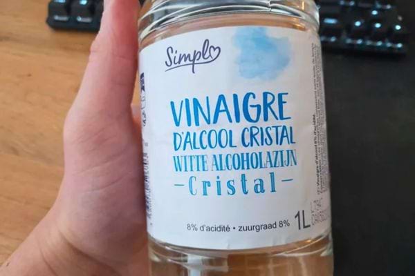 Main tenant une bouteille de vinaigre d’alcool cristal, utilisée pour le nettoyage ou la désinfection naturelle.