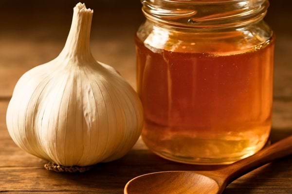 Une tete d’ail placee a cote d’un pot de miel.