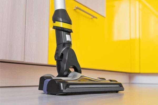 Un aspirateur sans fil nettoie le sol d une cuisine aux meubles jaunes.