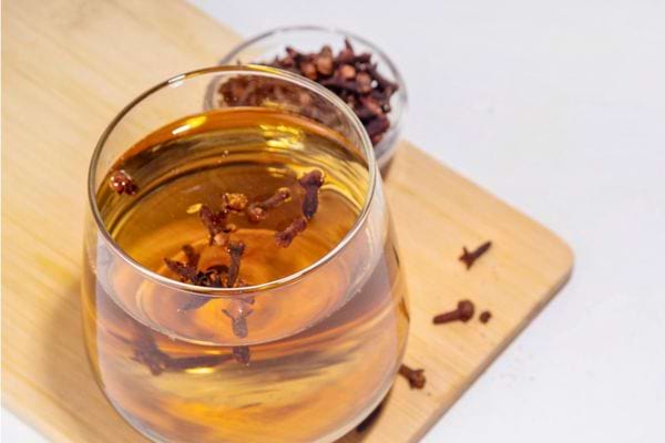 Verre contenant une infusion de clous de girofle sur une planche en bois.