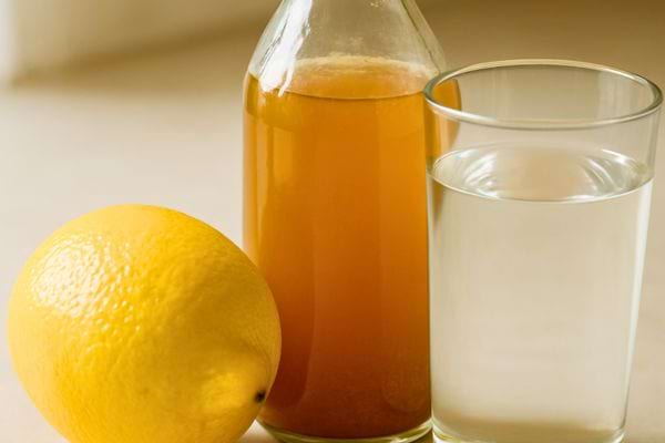 Un citron, une bouteille de vinaigre et un verre d’eau sont posés ensemble.