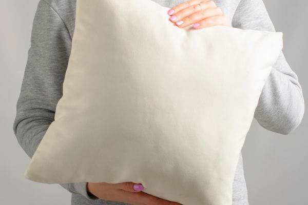 Personne tenant un grand coussin blanc avec les deux mains devant elle.