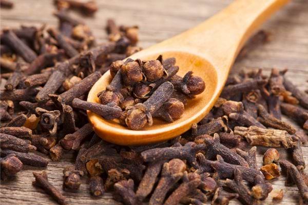 Cuillère en bois remplie de clous de girofle posée sur une table.