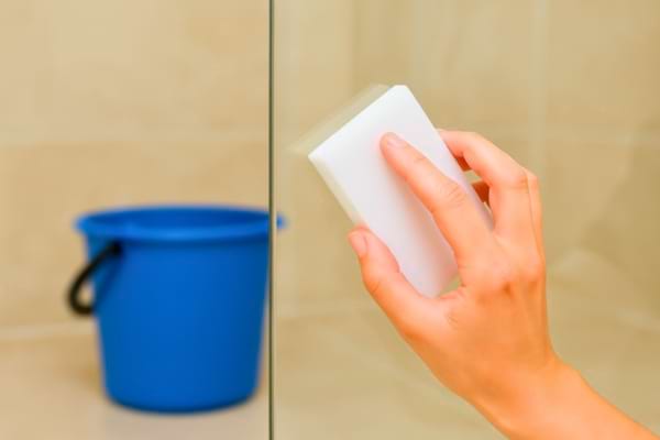 main d’un agent nettoyant une paroi de douche avec une éponge blanche humide