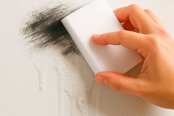 Une éponge magique efface une marque noire humide sur un mur clair.