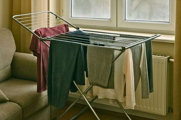 Un etendoir charge de vetements humide est place pres d une fenetre fermee.