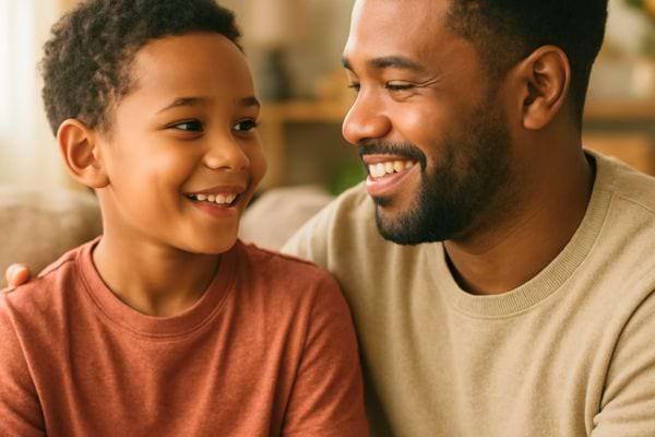 Un pere et son fils sourient en se regardant tendrement sur le canapé.