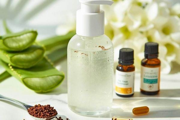 Flacon de gel transparent entouré d’aloe vera, huiles essentielles et cuillère de poudre végétale.